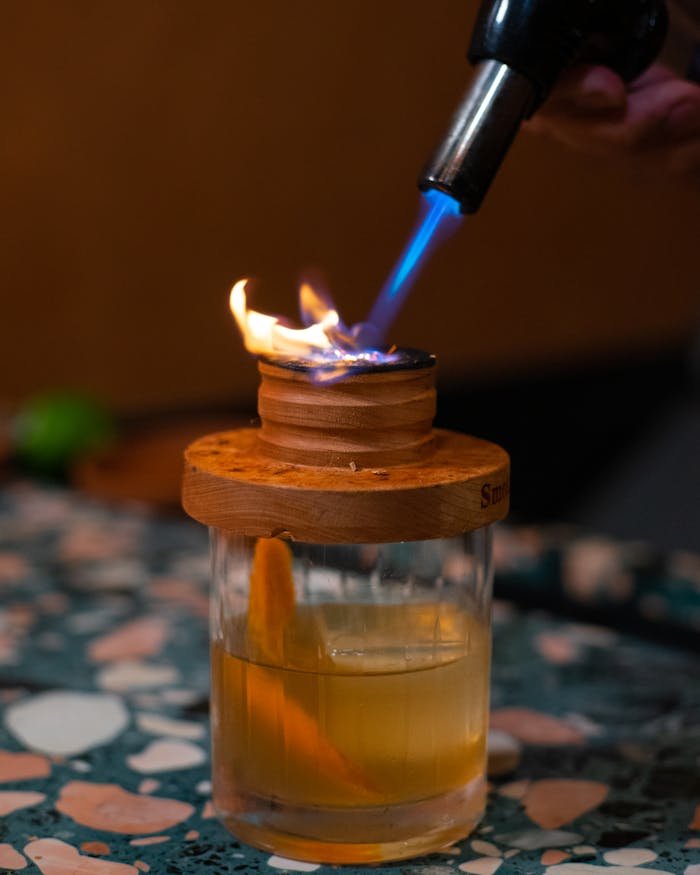 Close-up of a cocktail being flamed with a blowtorch on a patterned table.